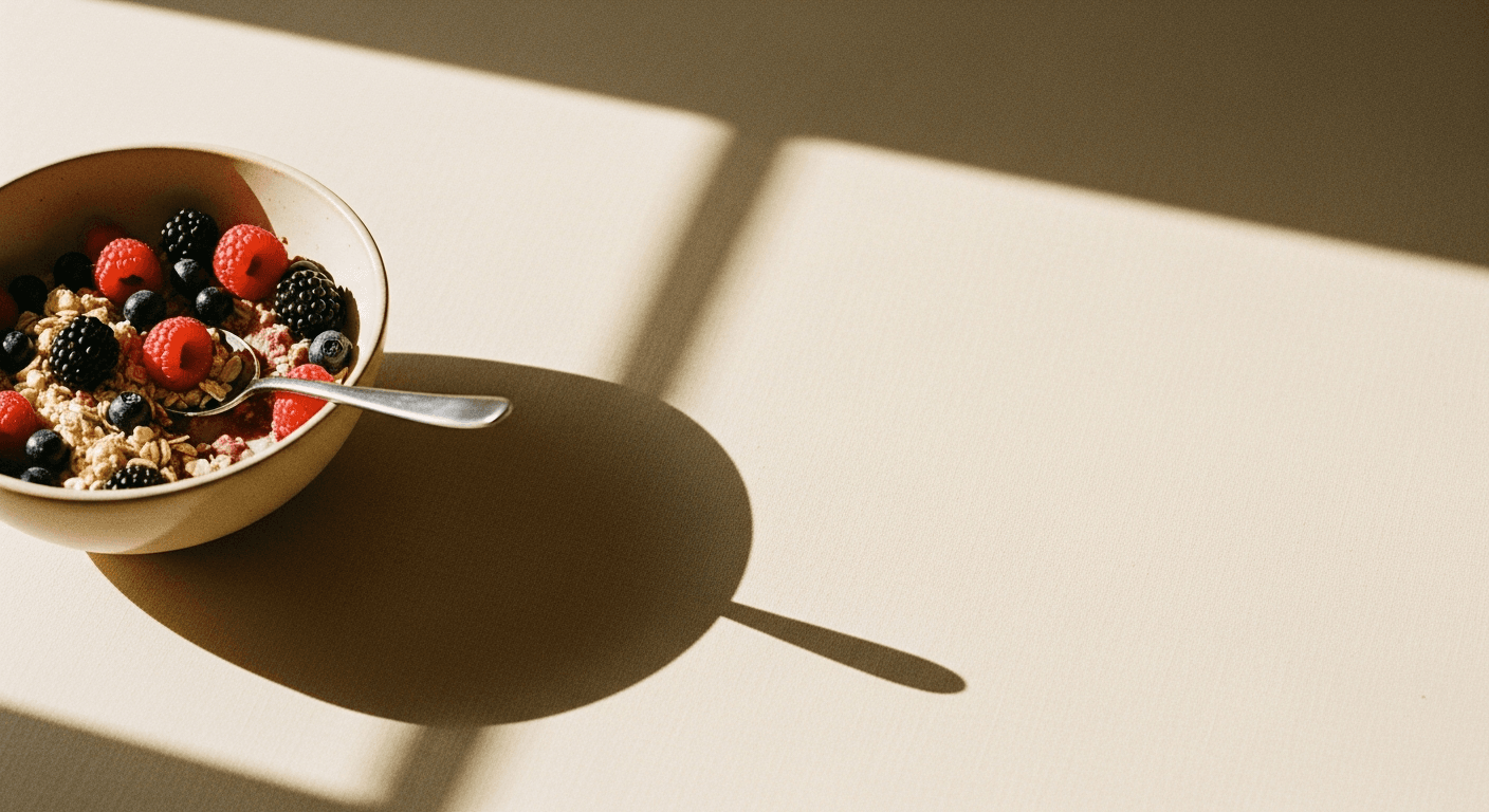 A half-eaten bowl of oats and berries in soft morning light casting diagonal shadows on cream linen.
