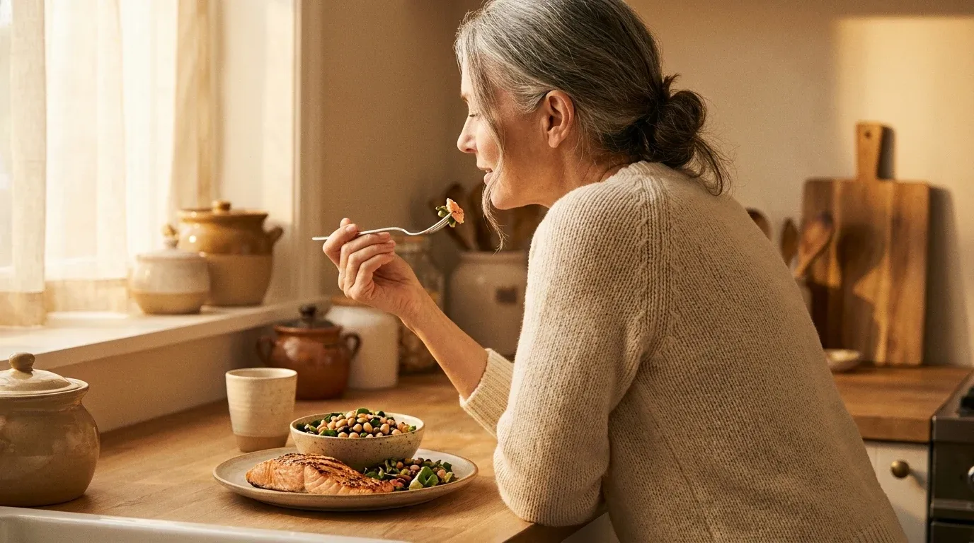 Mature woman tasting a high-protein meal at her kitchen counter in warm morning light.