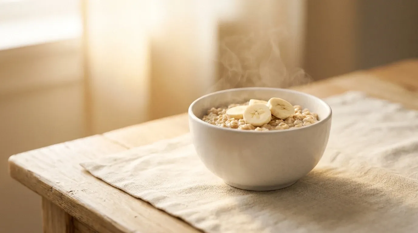 A simple bowl of oatmeal topped with banana slices on a wooden kitchen table in soft morning light.